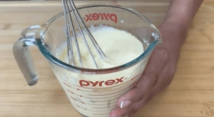 Whisking creamy batter in a Pyrex measuring cup on a wooden surface.